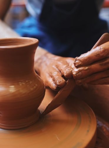 Potter using hand-tool for correcting edges of rotating jug